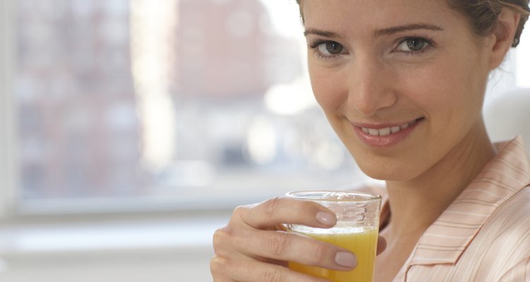 Young woman wearing pyjamas holding glass of juice, smiling, portrait