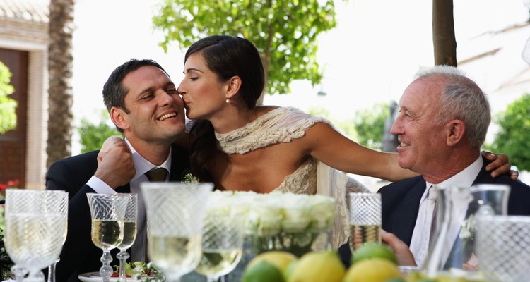 Bride kissing groom at table by father