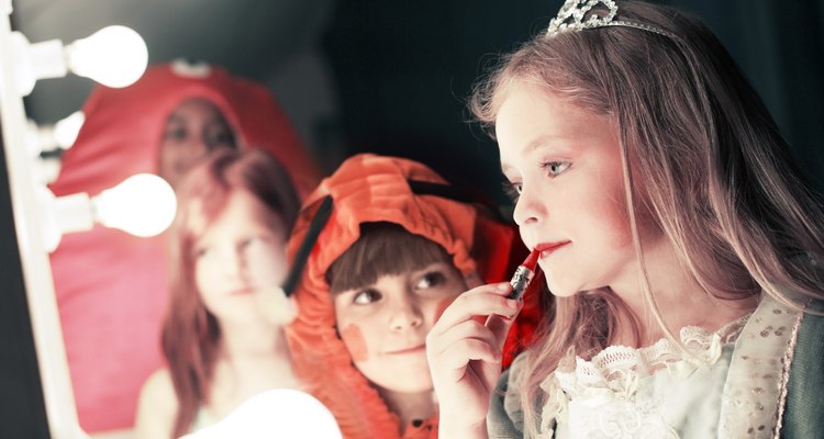 Two girls (5-8), one watching friend applying lipstick in stage mirror