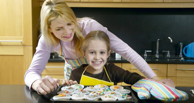 Mother and daughter (5-7) by baked cupcakes in kitchen, smiling