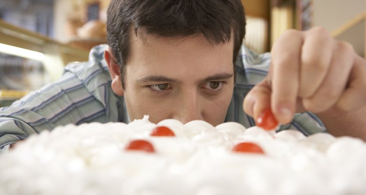 Young man putting cherry on top of cake, close-up