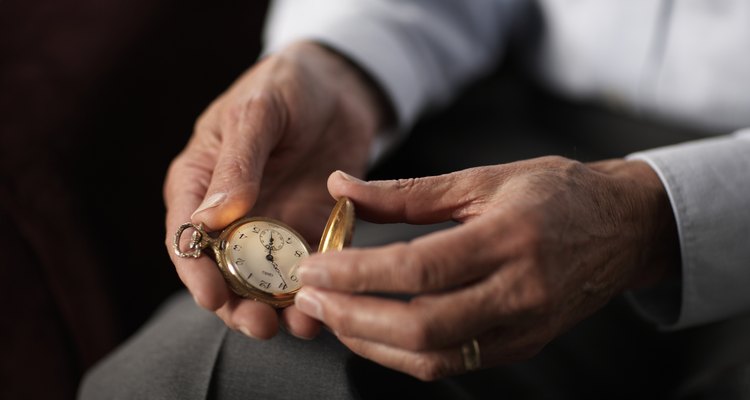 Senior man holding old pocket watch, mid section, close-up of hands