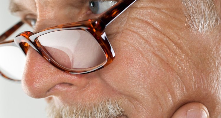 Close-up side view of a mature man rubbing his chin and looking over his reading glasses.