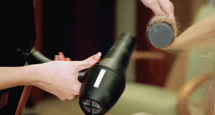 Close-up of a female hairdresser's hands styling a mid adult woman's hair