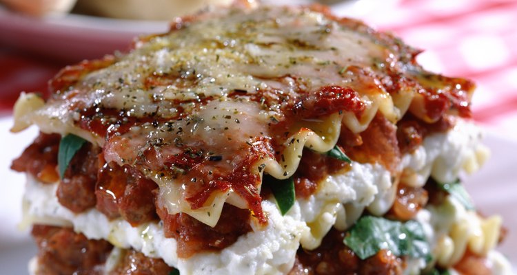 A close-up of a piece of lasagna and some breadsticks