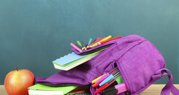 Purple backpack with school supplies on table of desk background