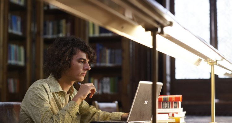 Young man sitting in libary using laptop, view under desk lamps