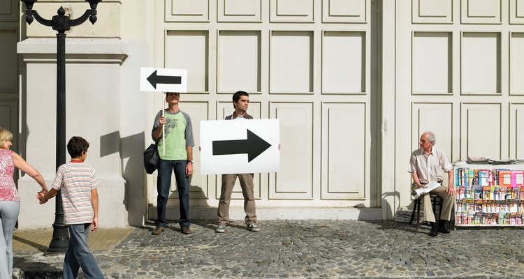 Two men holding arrow placards pointing in different directions