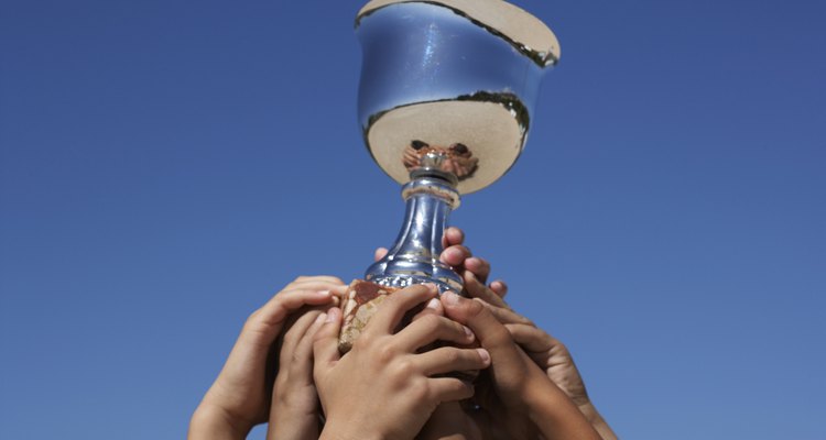 Close-up on raised hands holding trophy against blue sky