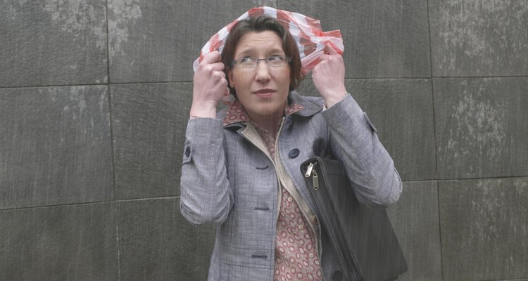 Businesswoman standing in rain holding plastic bag over head