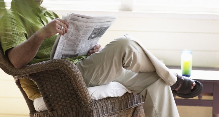 Mature man sitting on wicker rocking chair, reading newspaper