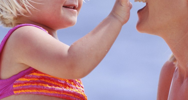 Girl (2-3) applying sunscreen on mothers nose, on beach