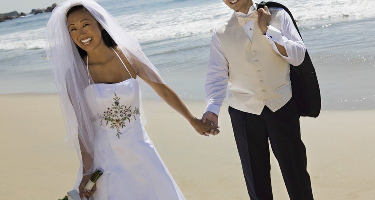 Bride And Groom Holding Hands While Walking On Beach