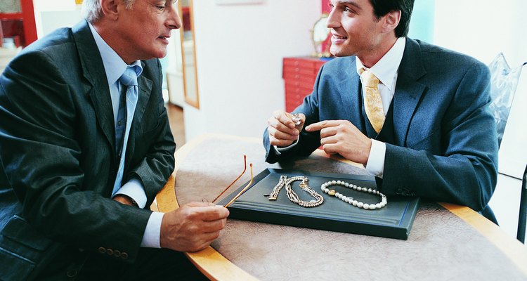 Man Sitting at a Table Opposite a Shop Assistant in a Jewellery Shop Looking at Necklaces and Rings
