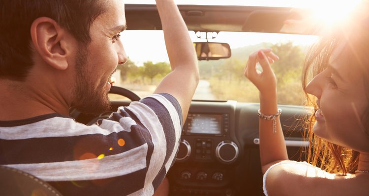 Young Couple Driving Along Country Road In Open Top Car