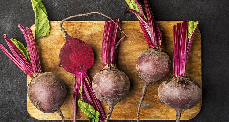 Raw organic farm beetroot on a vintage wooden cutting board on a plain black background. Top View.