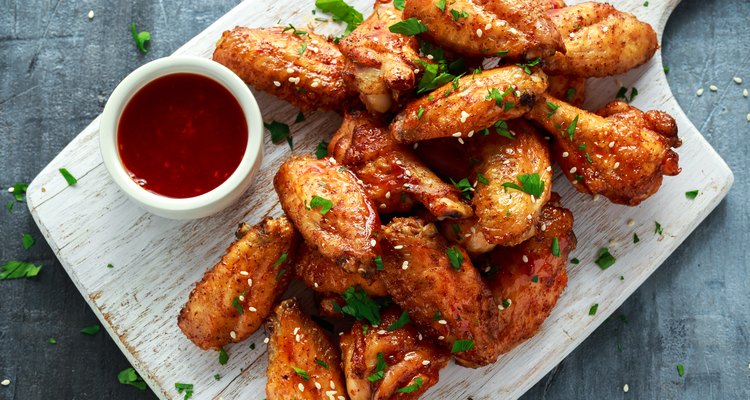 Baked chicken wings with sesame seeds and sweet chili sauce on white wooden board.