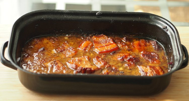 Baked pork belly with a sauce in a black roasting pan on a wooden table. Traditional specialty form the Czech Republic called 'moravsky vrabec'.