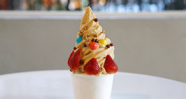 Closeup Cup of Organic Frozen Yogurt Ice cream, Salted Caramel Pecan with fresh strawberry and chocolate candy in a plastic takeaway on blurred background.