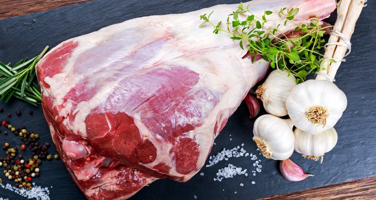Raw lamb leg on blue stone background with herbs