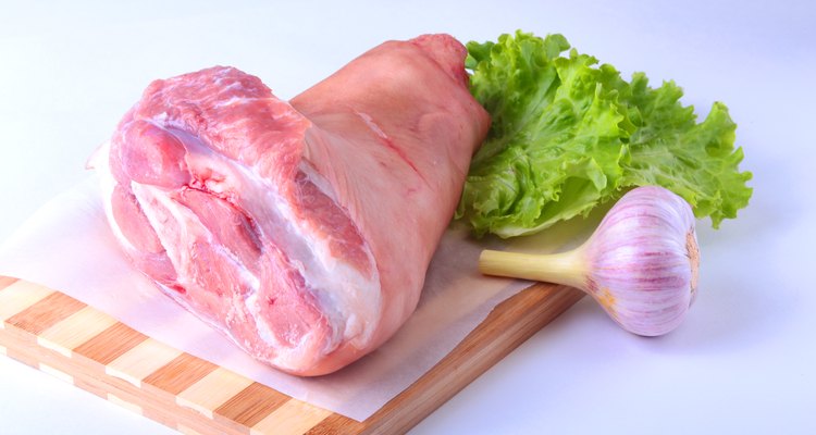 Raw pork knuckle, garlic and lettuce leaves on a cutting board. Selective focus. Ready for cooking.