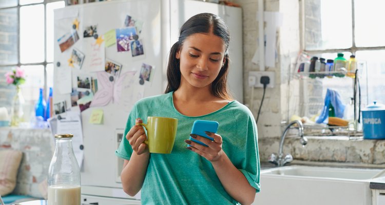 Woman holding coffee using blue mobile phone at home