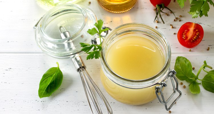 Homemade salad dressing vinaigrette with mustard, olive oil, lemon juice and various fresh vegetables and herbs on a wooden background. The concept of a healthy diet and detox diet.