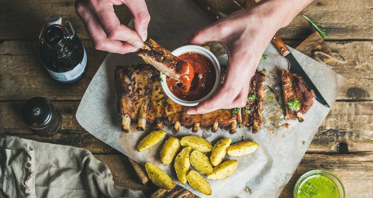 Man's hands dipping piece of roasted pork to ketchup