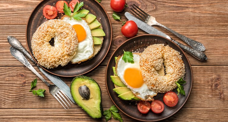 Bagel with avocado and egg on the wooden background.
