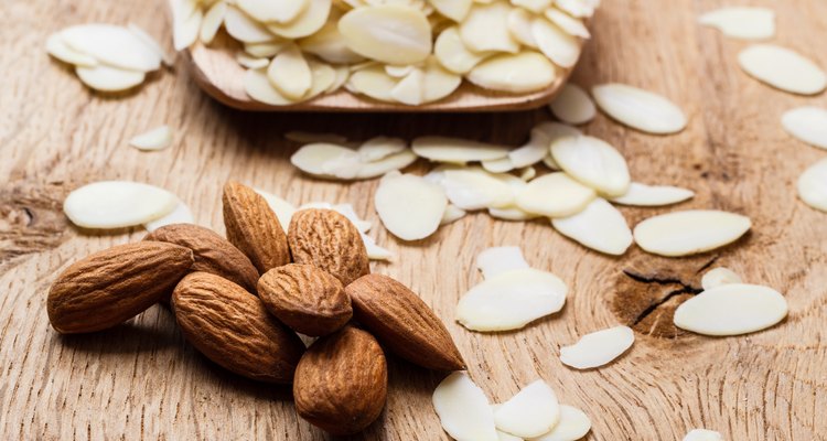 sliced and whole raw almonds on wooden surface