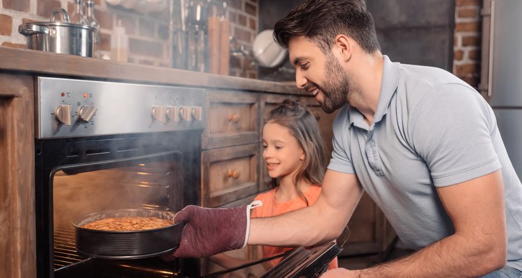 smiling father and daughter taking cake from oven