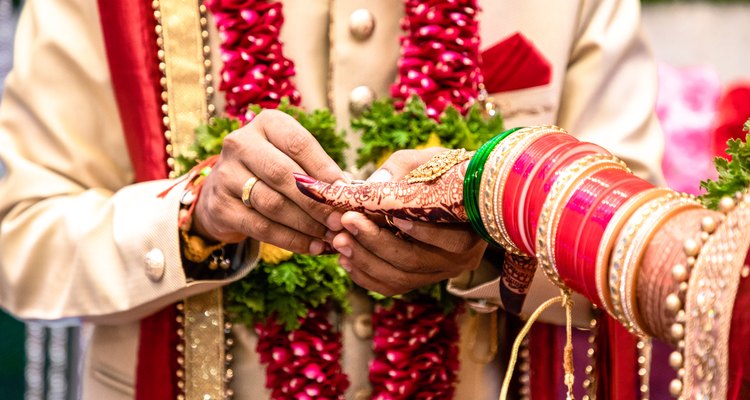 Engagement Ring ceremony- Indian Hindu male putting ring on bride's decorated finger. Couple is well attired as per traditional Indian Hindu wedding. Groom wearing Jodhpuri suit and floral garland.