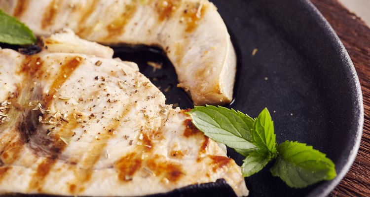 grilled swordfish slices in a cast iron pan on a wooden table, garnished with mint, oregano, salt and salmoriglio