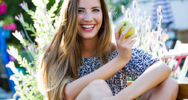 Beautiful young woman eating an apple in the home garden.