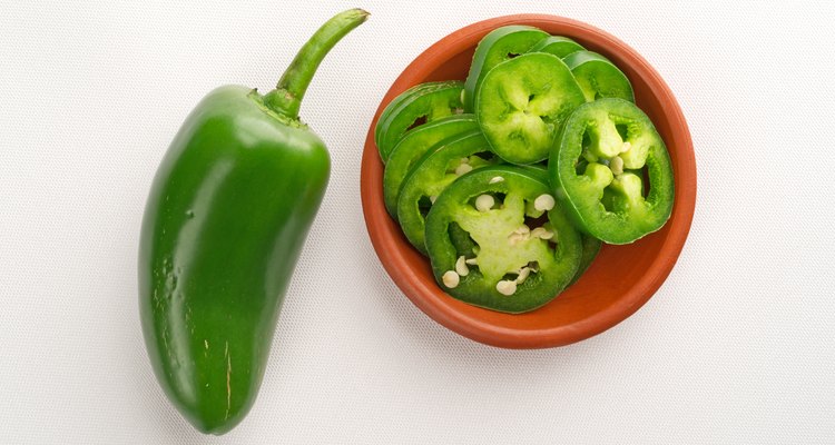 Sliced jalapeno peppers in bowl with pepper to side