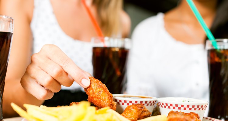 Two women eating chicken wings and drinking soda