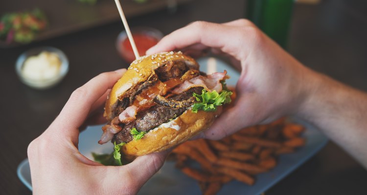 man holds burger with hands and sweet potato fries