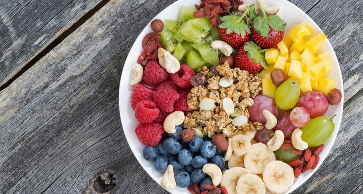 Mixed fruit, nuts and granola in a white bowl on wood table