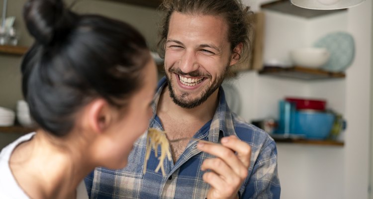 Young couple preparing food together, tasting spaghetti