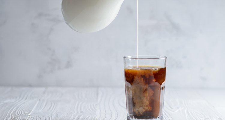 Iced coffee with pouring milk in glass