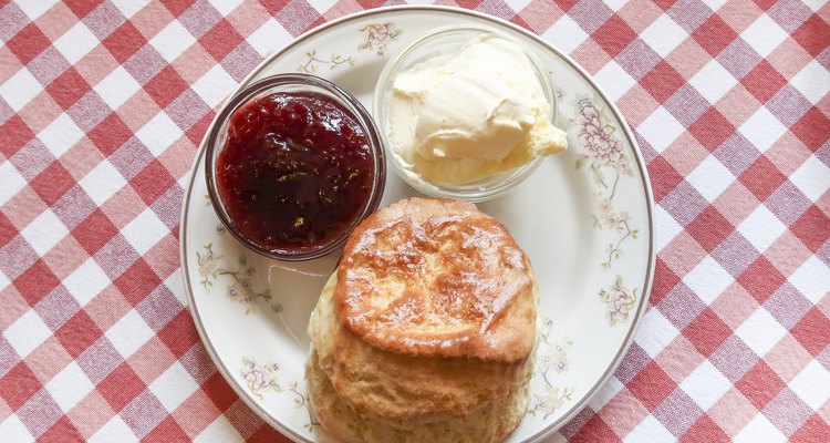 Scone and strawberry jam and clotted cream on a plate on a table with a red and white checkered table cloth