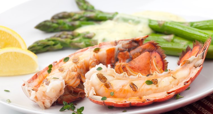 Grilled lobster tails on a plate wit asparagus and lemon wedges