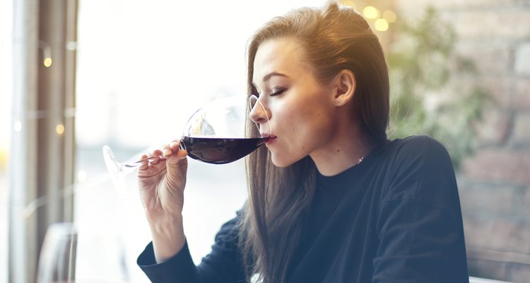 Beautiful young woman drinking red wine with friends in cafe, portrait with wine glass near window. Vocation holidays evening concept