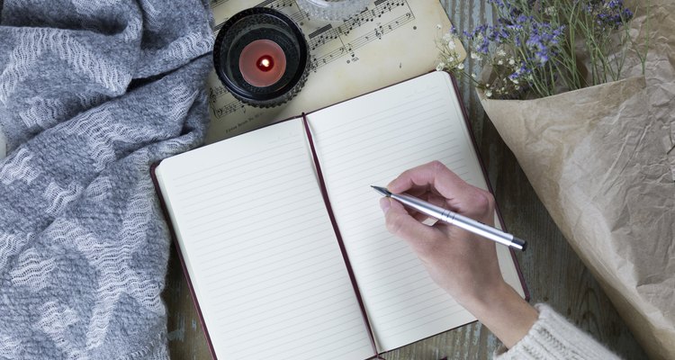 woman's hand writing in notebook near candles and flowers