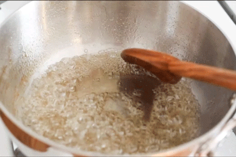 A wooden spoon stirring bubbling simple syrup in a saucepan.