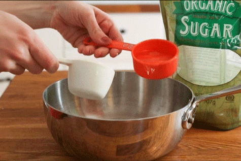 A cook adding equal parts sugar and water to a saucepan