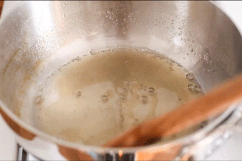 A wooden spoon stirring sugar glaze in a saucepan.