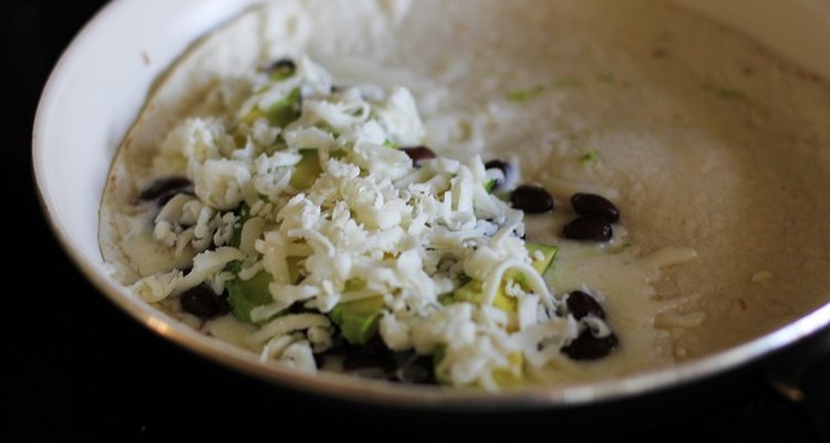 Half of a flour tortilla covered with black beans, avocado and cheese.