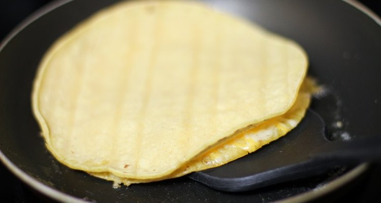 Spatula beneath a quesadilla cooking on a skillet.