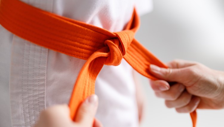 The coach's caring hands are tying the belt on the children's kimono.